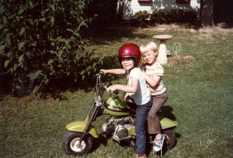 Wright as a kid in a red helmet on a green minibike, with a friend riding on the back